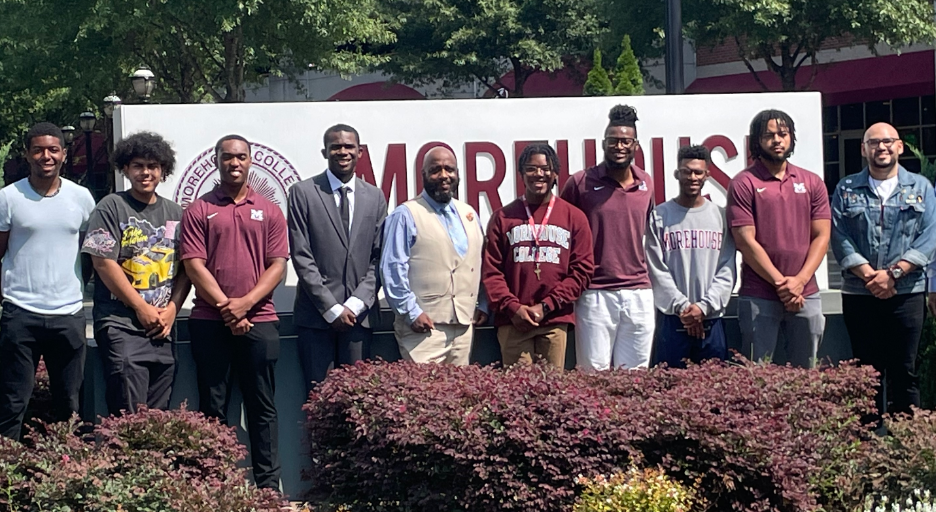 A group of men standing in front of a sign

Description automatically generated